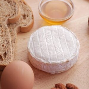 Image of a wheel of brie next to bread, an egg, and honey.